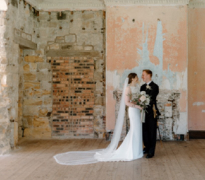 A couple on their wedding day standing in front of a shabby-chic internal wall
