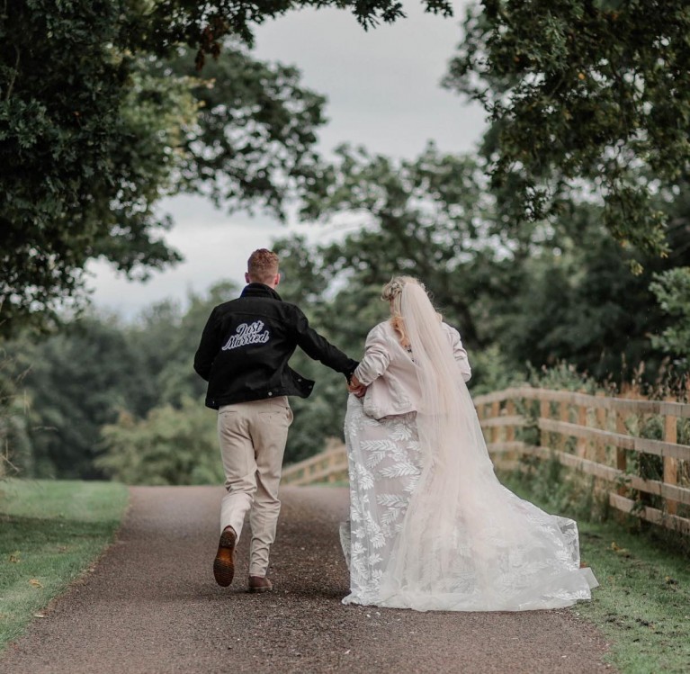 A bride and groom running down a country road