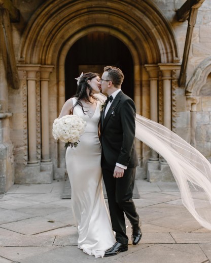 A bride and groom kissing by a fence in front of foliage