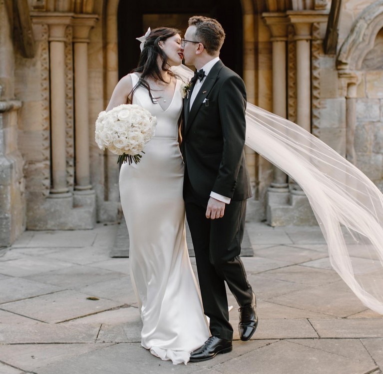 A bride and groom kissing in front of Brinkburn Priory in Northumberland
