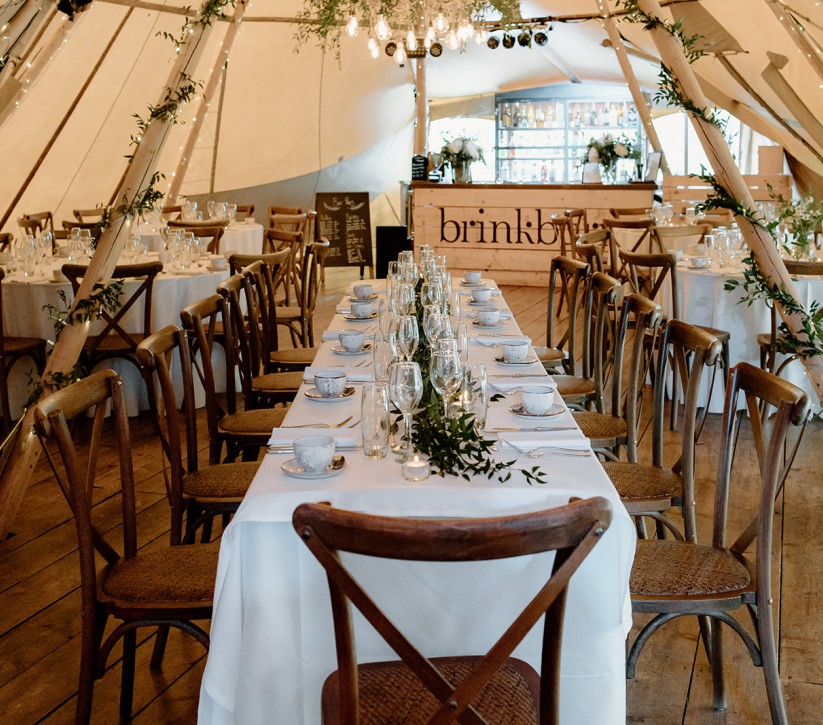A large white dining table in a giant tipi with a bar in the background